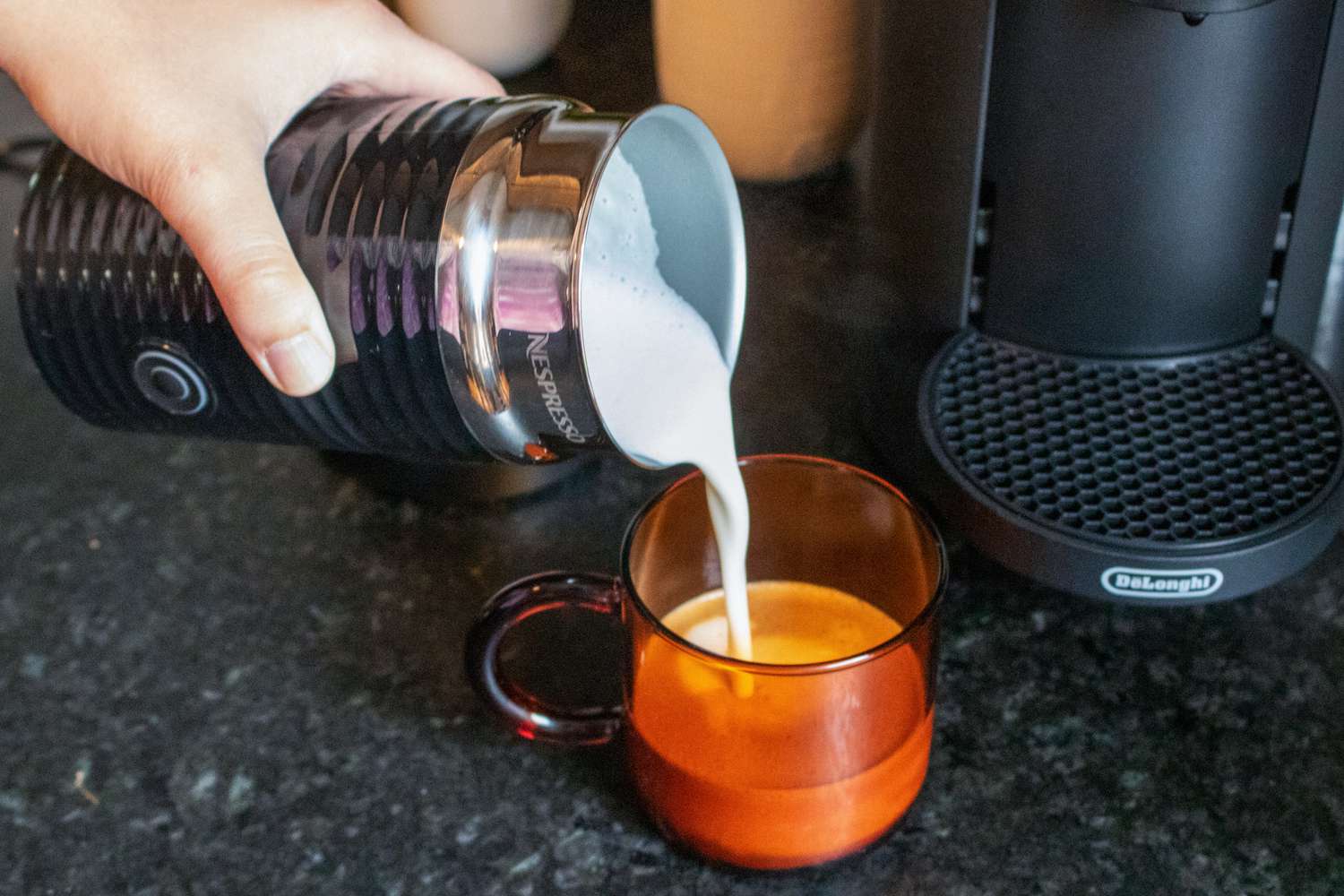 The Nespresso milk frother pouring frothed milk into a mug with brewed coffee