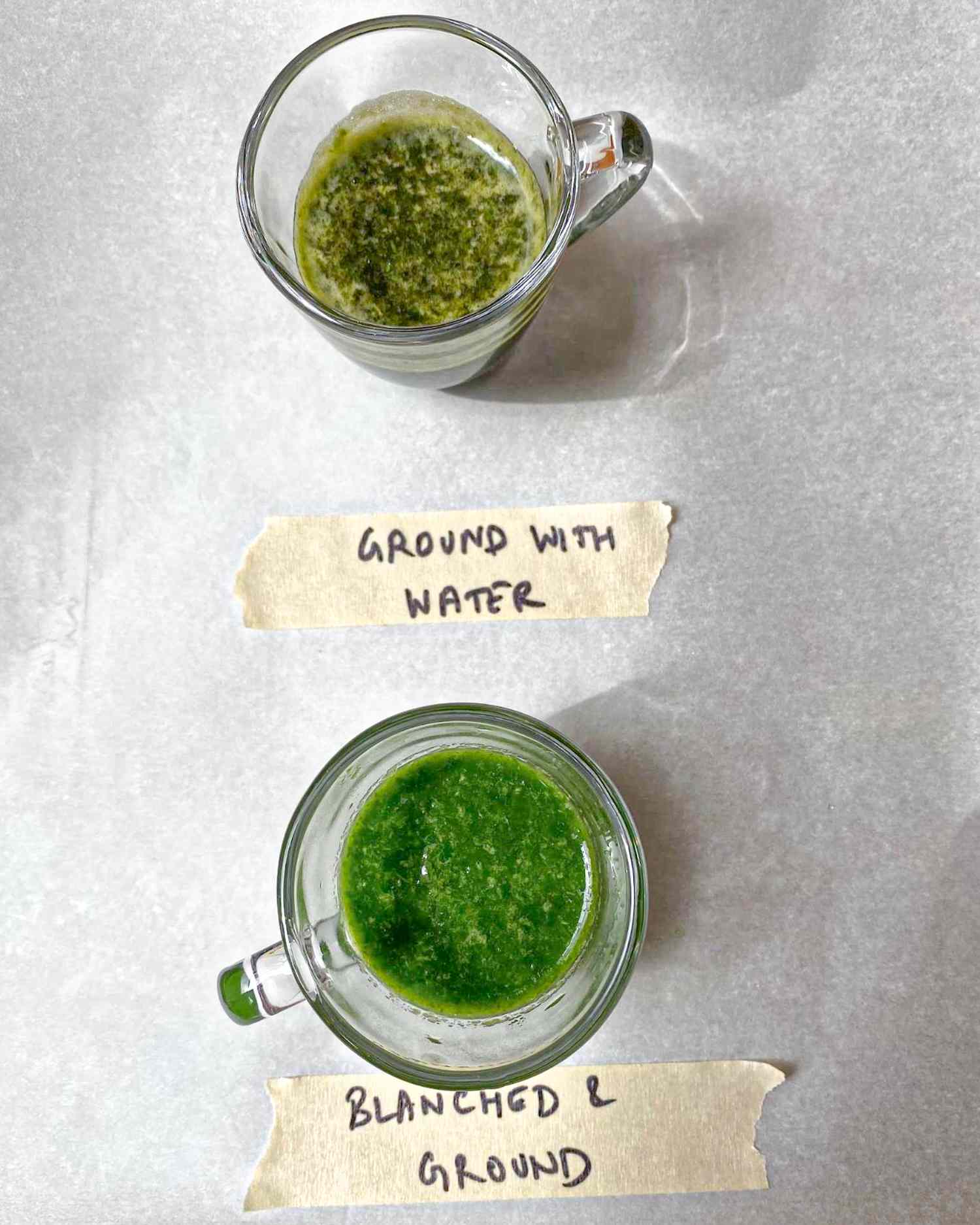 Two small clear containers with pesto labeled as Ground with Water and Blanched and Ground arranged on a surface