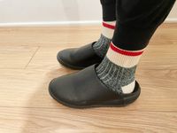 A person wearing a pair of black Snibbs clogs with socks on.