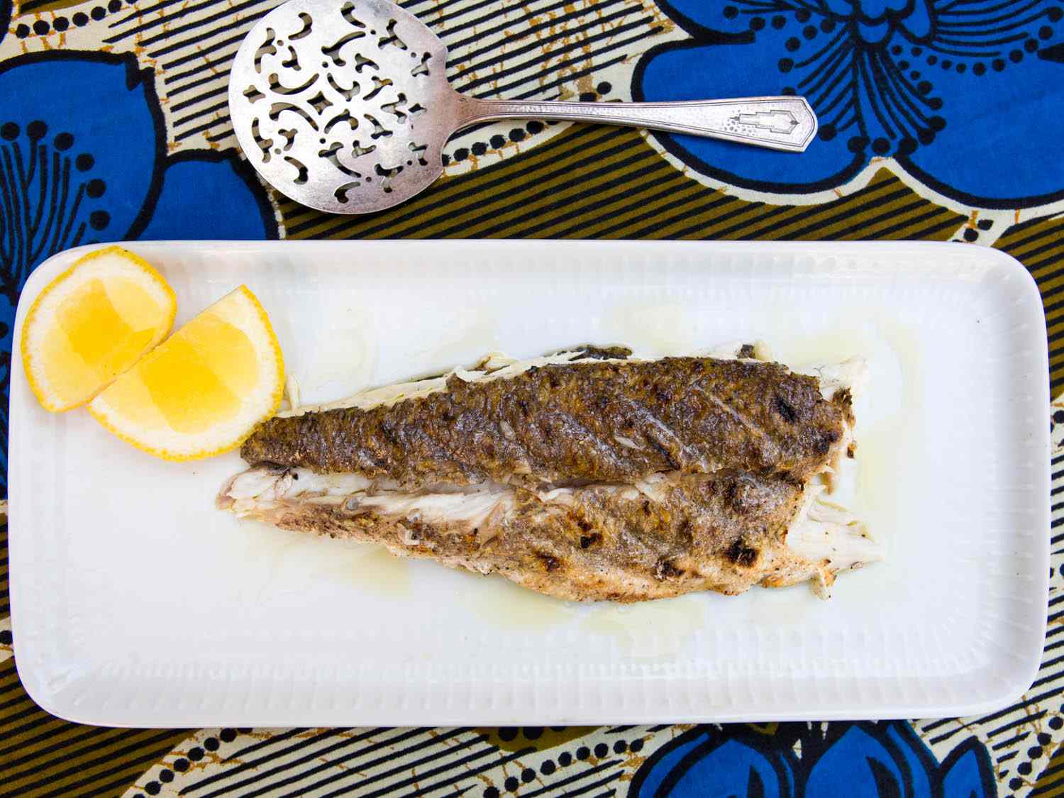 Overhead view of the carved fish fillet, served on a rectangular platter with lemon quarters.