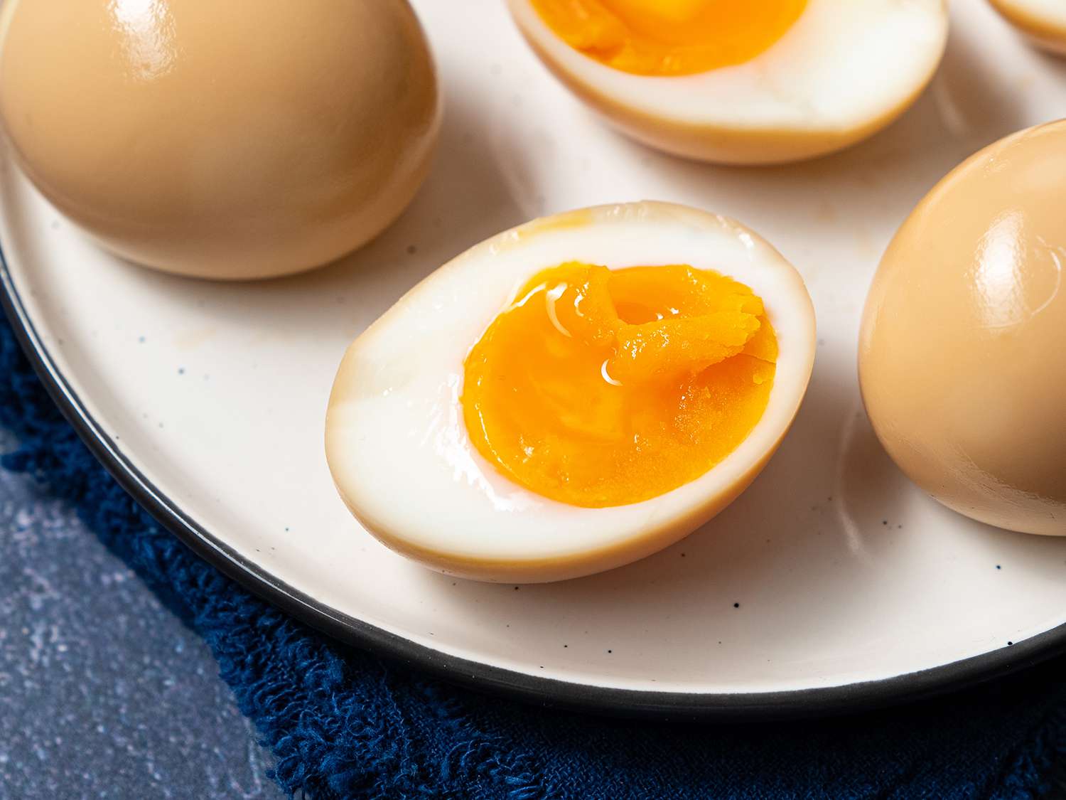 Soft boiled eggs for ramen on a plate. One has been cut upon to reveal the jammy yolk. 