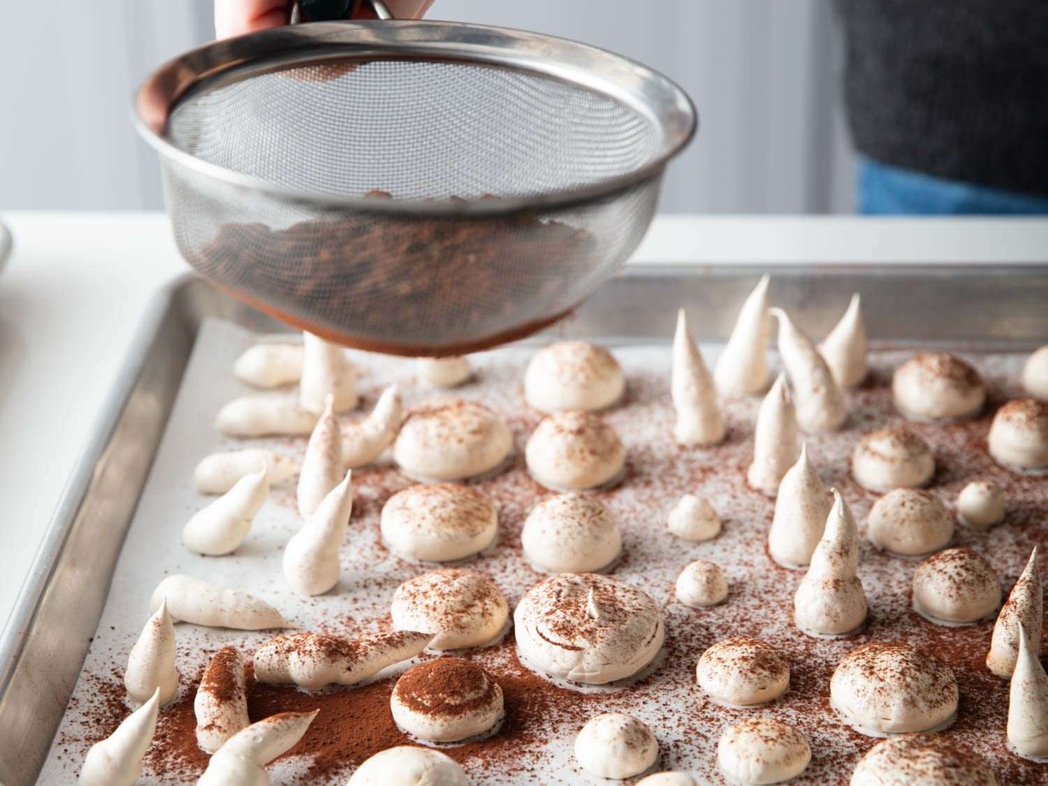 Dusting the meringue mushroom caps and stems with cocoa.