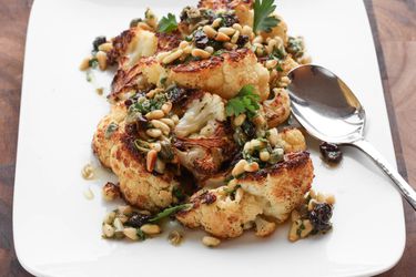 Closeup of Roasted Cauliflower With Pine Nut, Raisin, and Caper Vinaigrette, served on a square white plate.