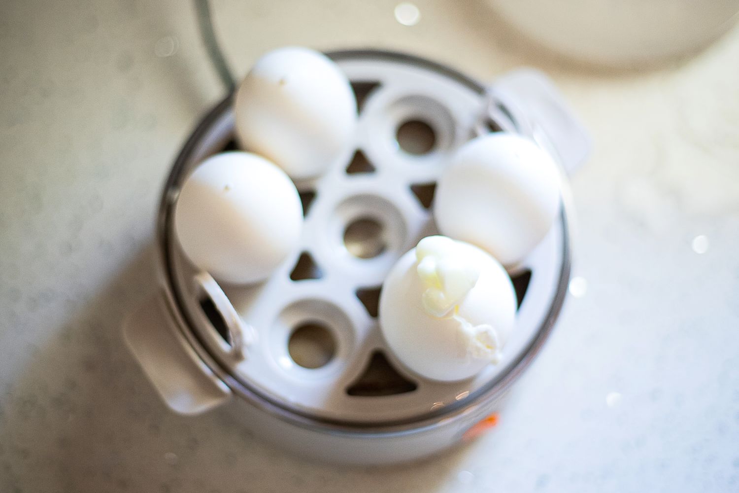 An egg in an egg cooekr with the white bubbling out of the shell