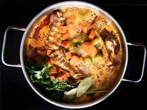 Overhead view of roasted turkey bones, browned vegetables, and herbs simmering in stockpot
