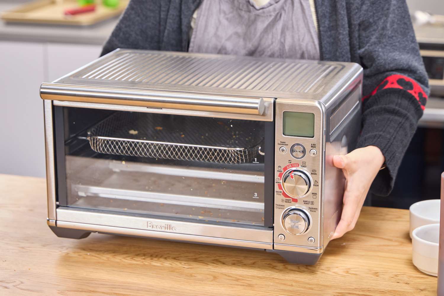 A person places the Breville The Smart Oven Air Fryer Compact onto a countertop