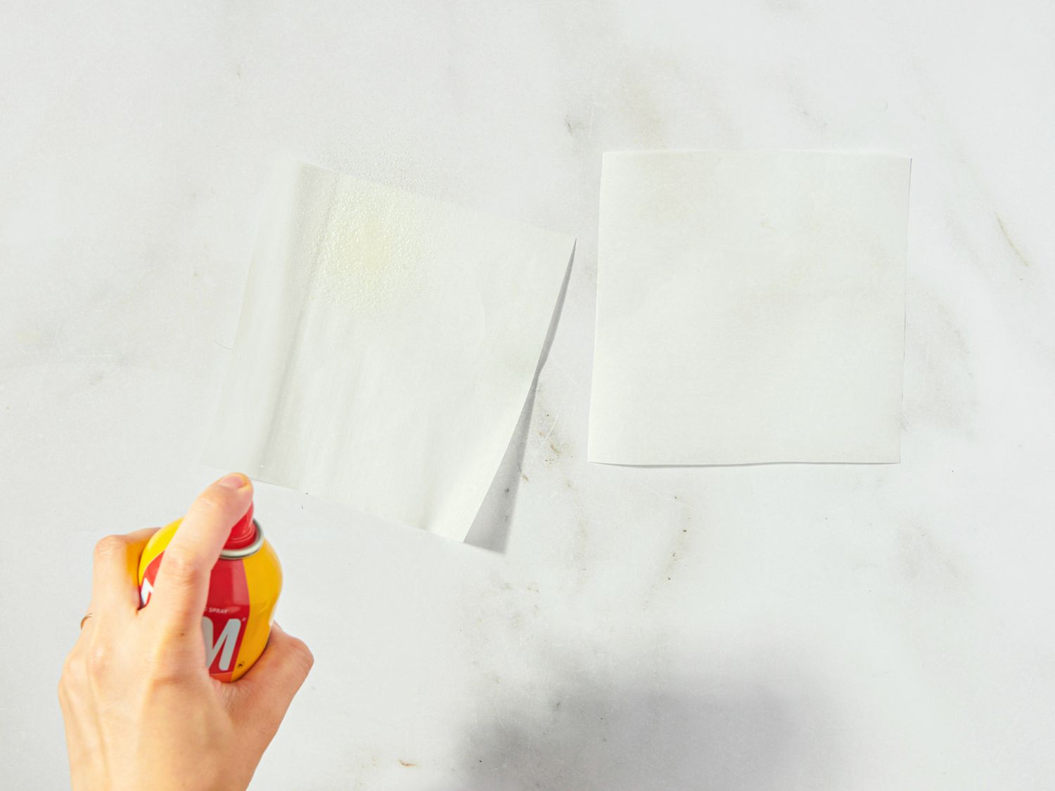 Person spraying nonstick cooking spray on a piece of parchment paper