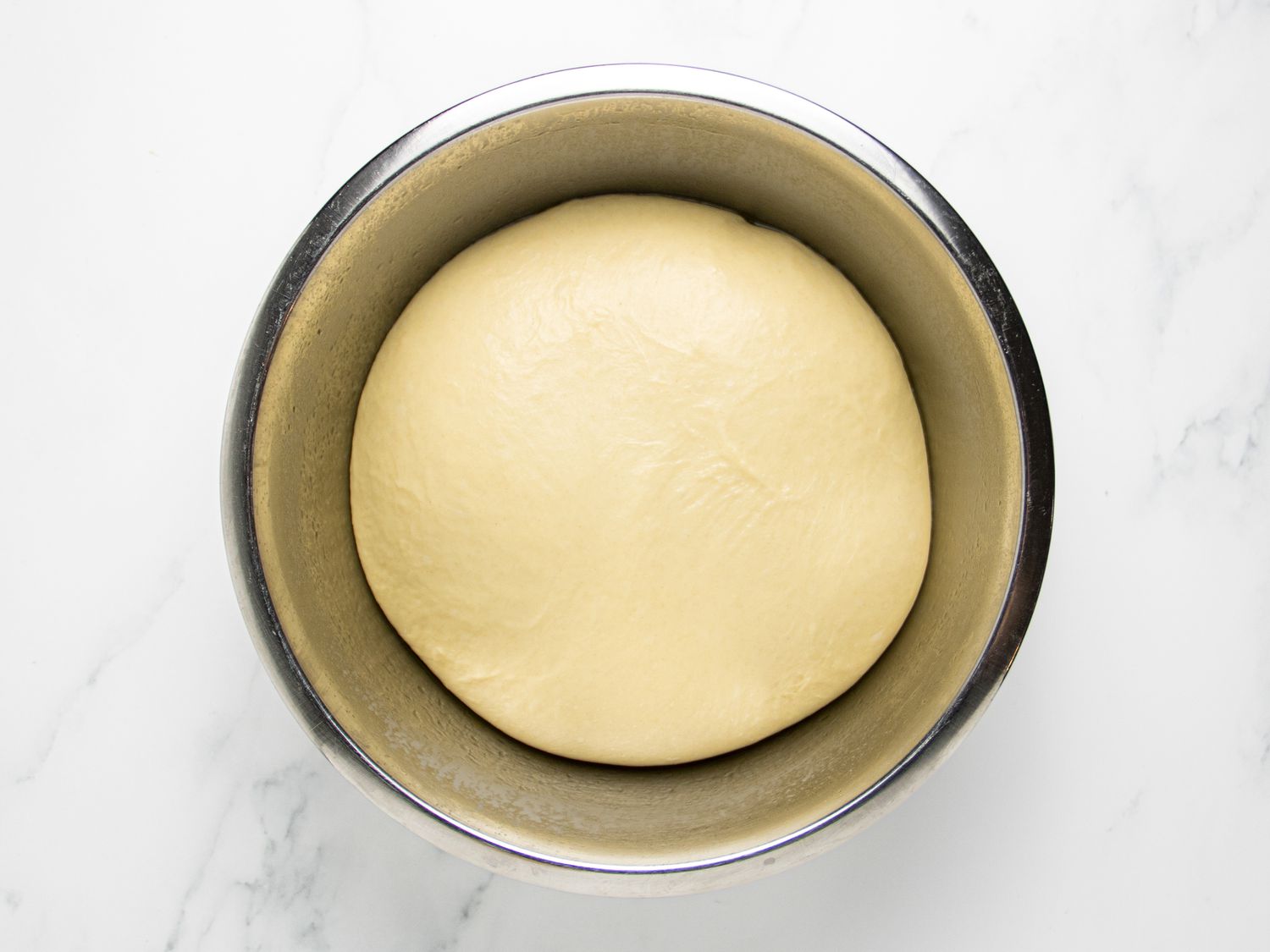 Dough proofed in a bowl on a marble surface