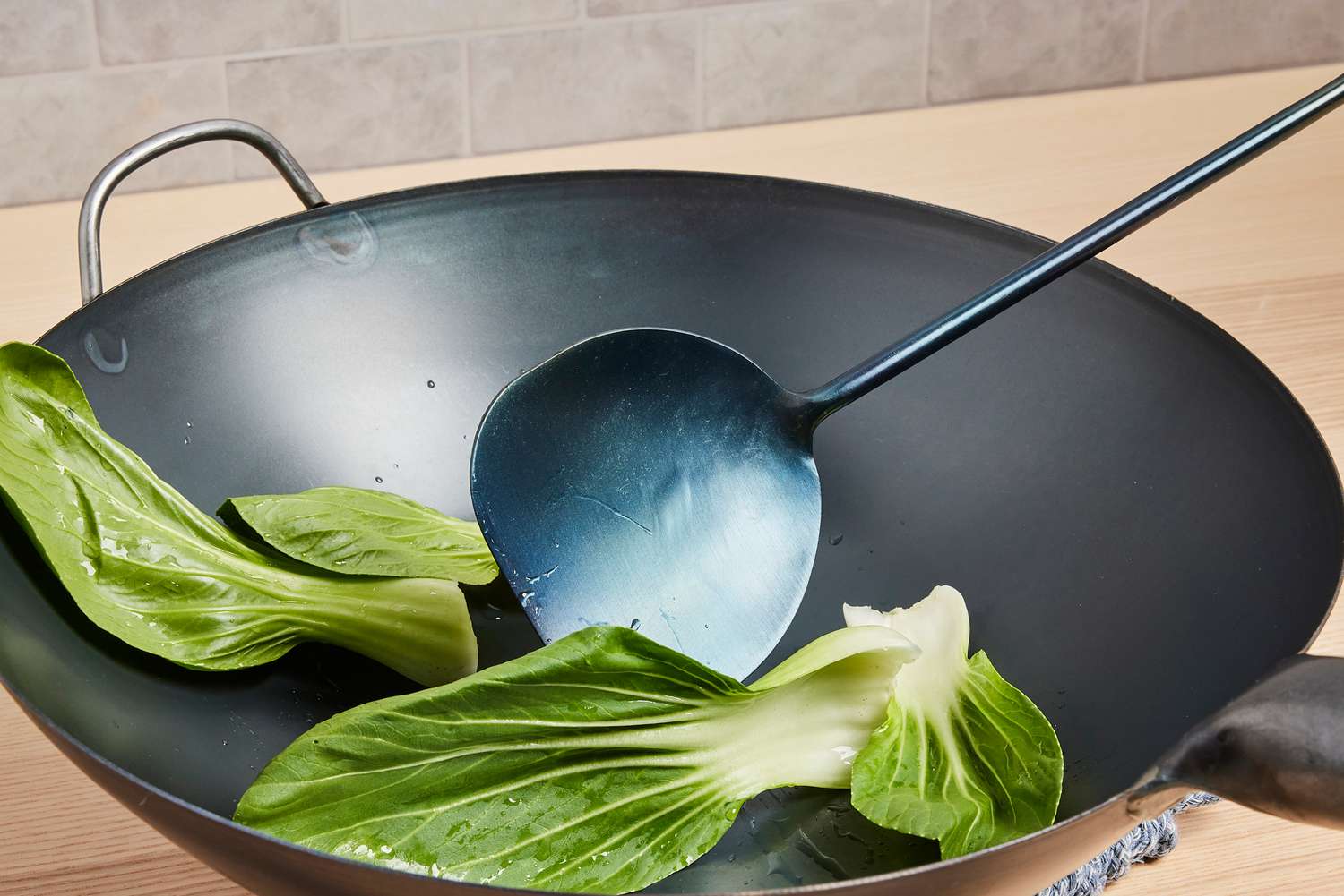 using a wok chuan to toss bok choy in a wok