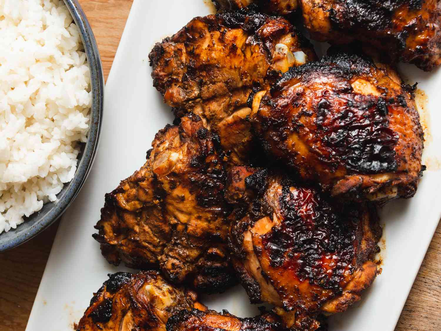A platter of grilled tamarind chicken thighs next to a bowl of white rice.