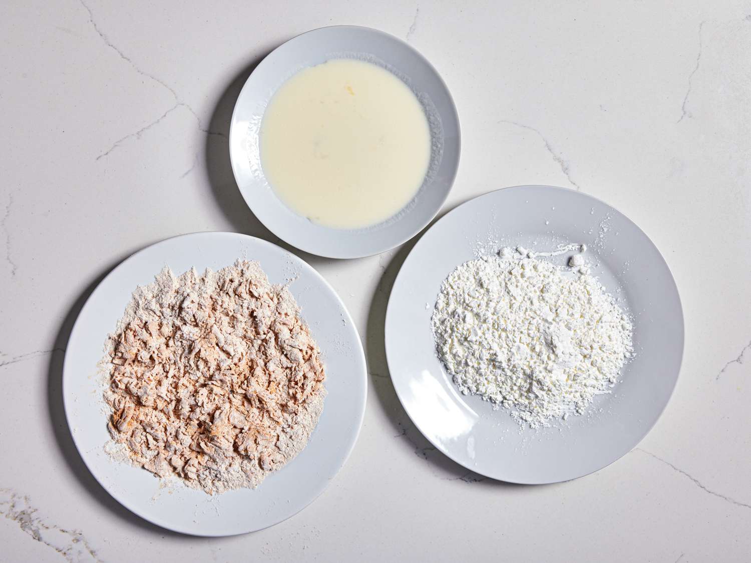 Three white bowls with egg, flour, and bread crumbs