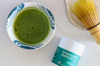 An overhead shot of a glass of Rishi Tea Everyday Matcha next to the container