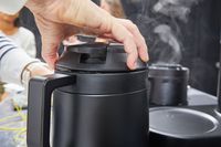 A hand unscrewing the lid on the Ratio Six Coffee Maker's carafe.