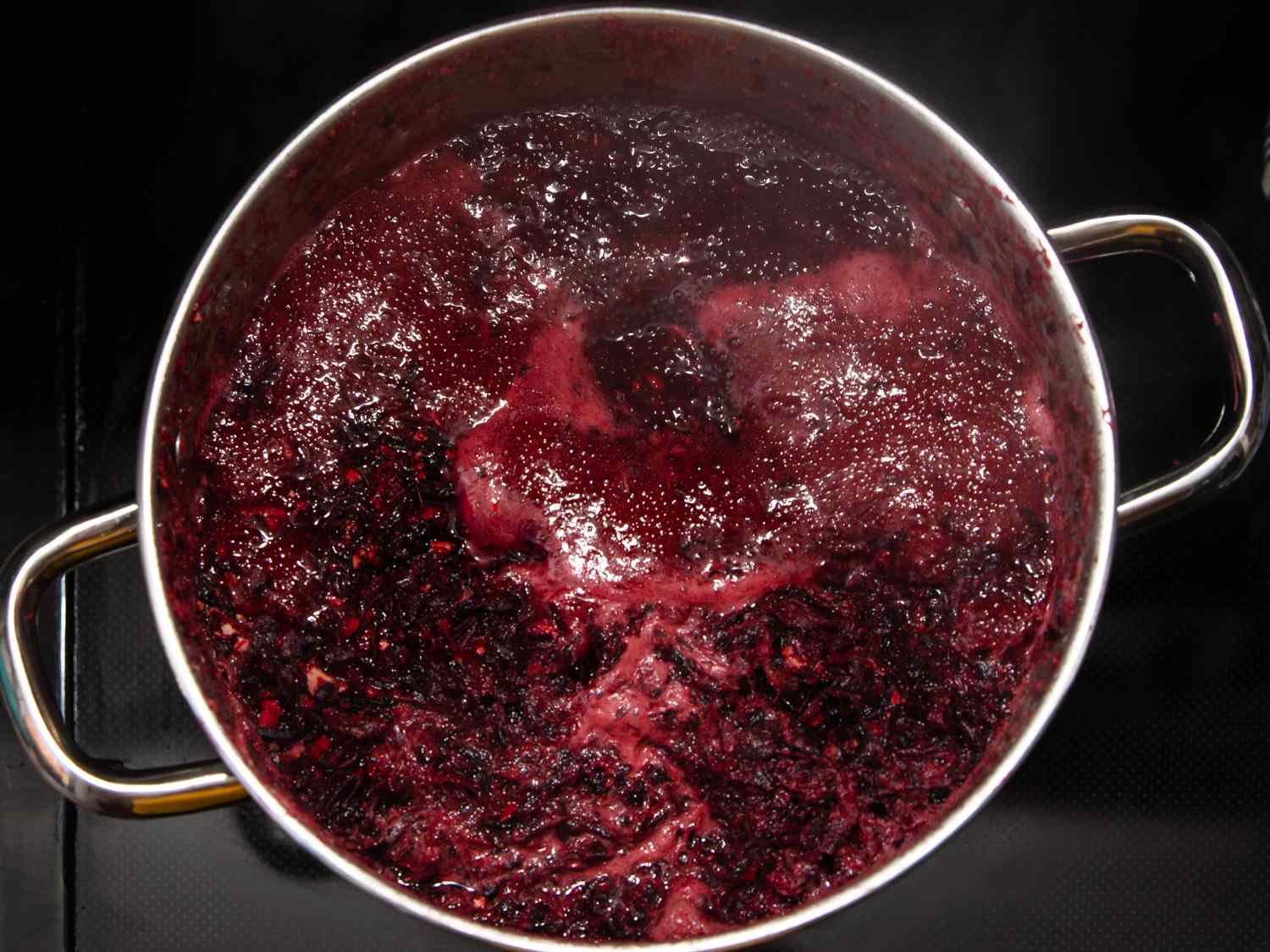 Water, sorrel, grated ginger, cloves, and crushed allspice boiling in a pot.