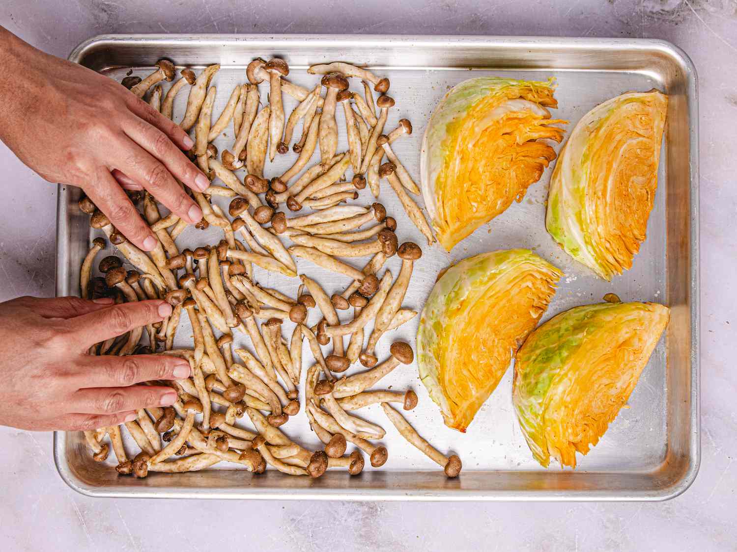 A tray of enoki mushrooms and cabbage wedges being arranged by hands