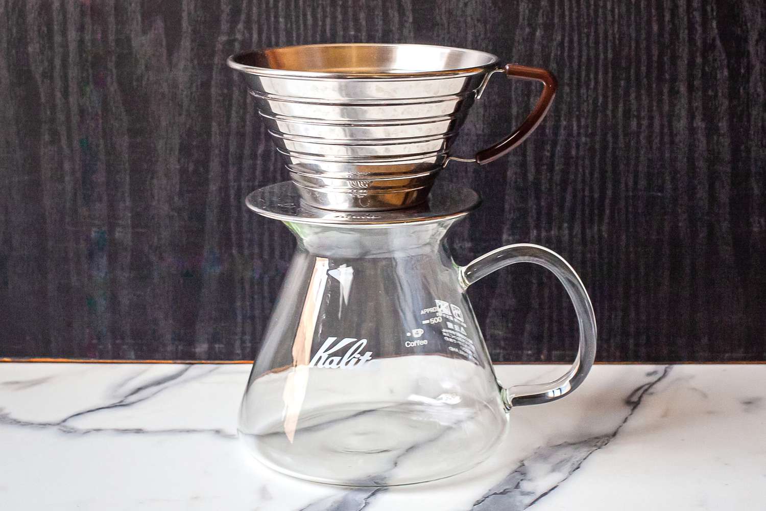 A metal coffee dripper sitting on a glass carafe