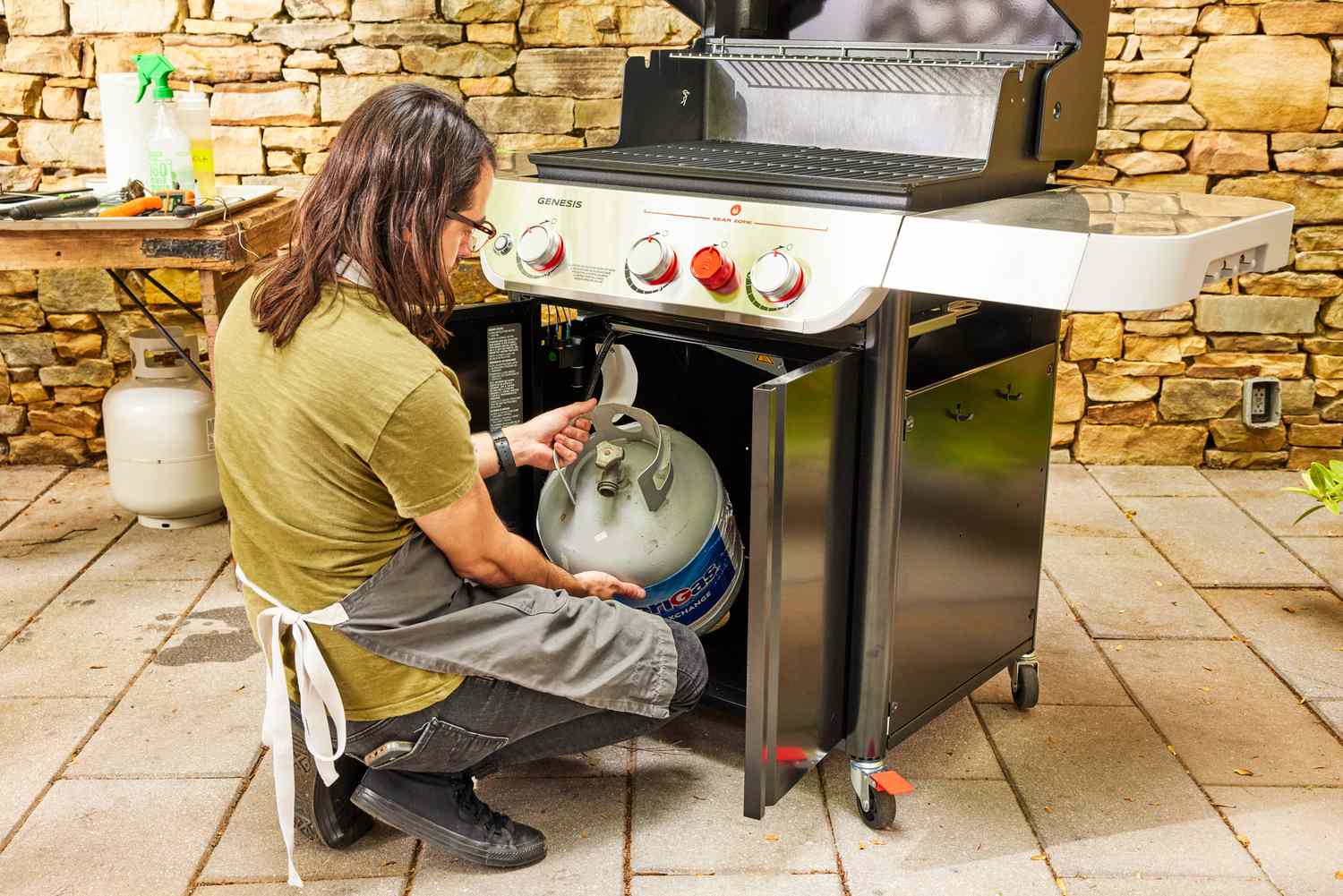 A person places a propane tank into the Weber Genesis E-325 Liquid Propane Gas Grill