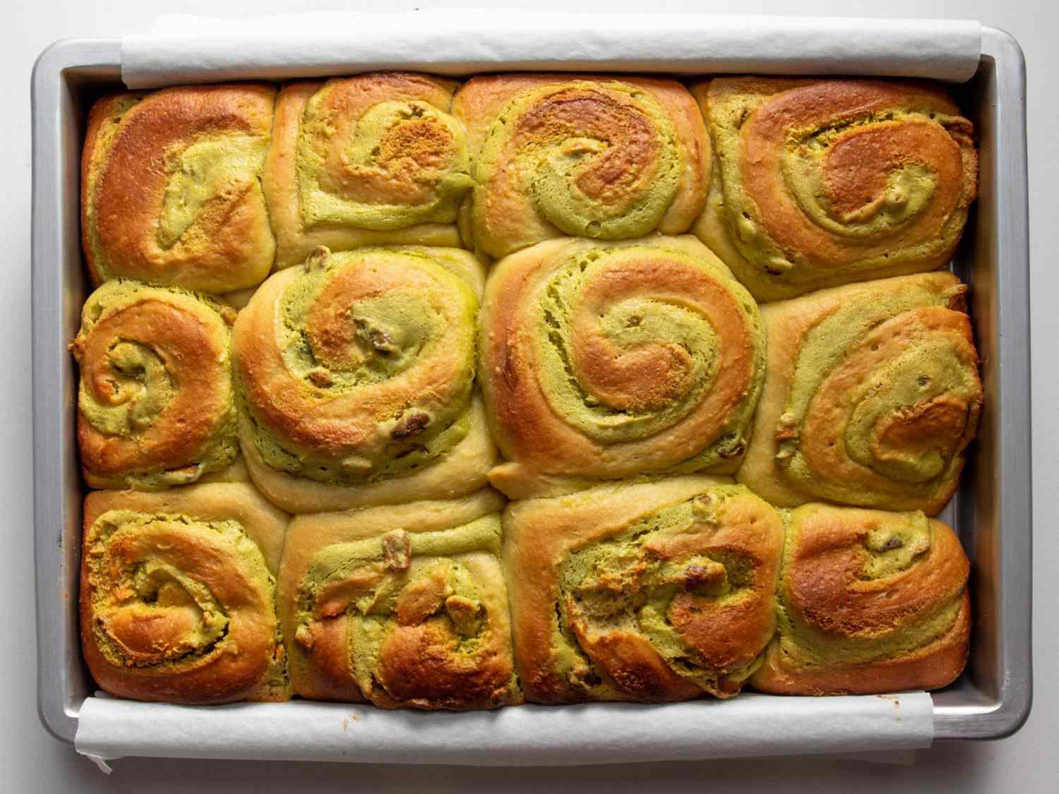 A dozen fully baked pistachio buns arranged in a baking pan. 