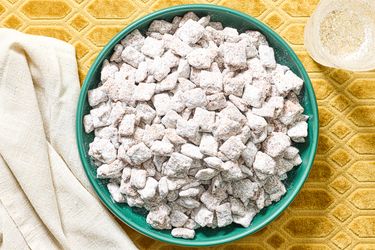 A bowl of powdered sugarcoated snack mix on a textured surface