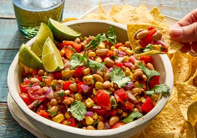 A bowl of cowboy caviar surrounded by tortilla chips with a hand holding a chip topped with the dish