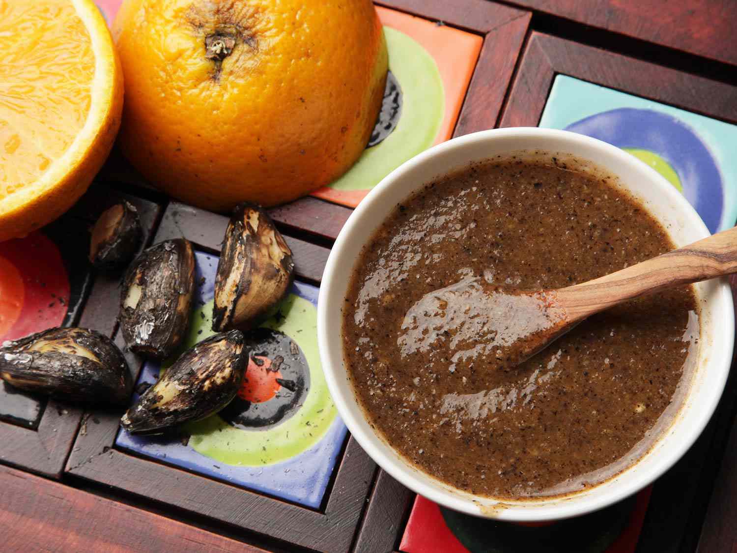 A dish of chile tamulado (spicy Yucatecan habanero salsa) next to orange halves and charred garlic cloves