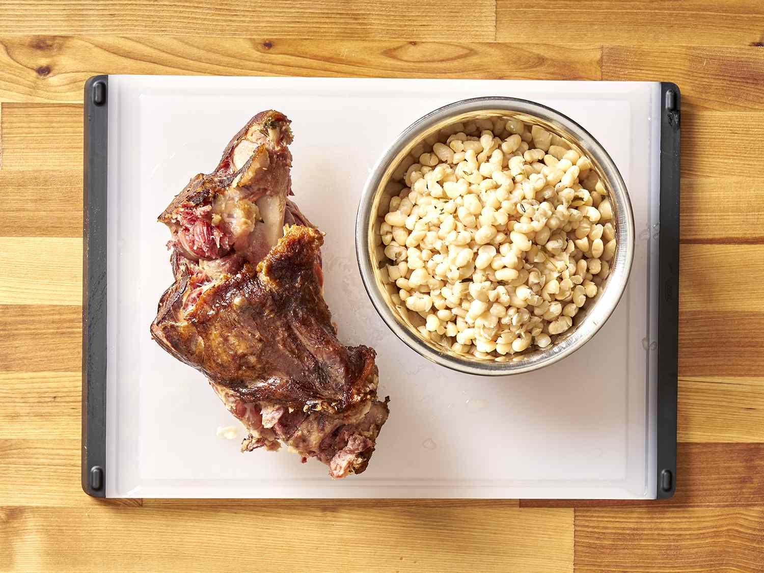 Ham hock and navy beans resting on a cutting board.