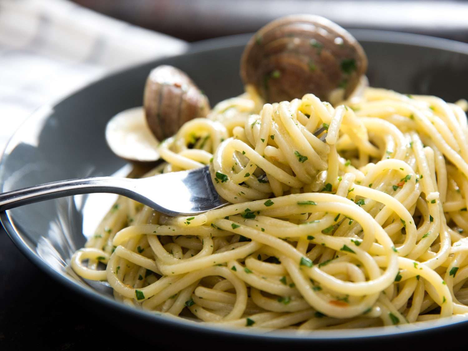 A fork twirled into spaghetti alle vongole in bianco with clams in the background.