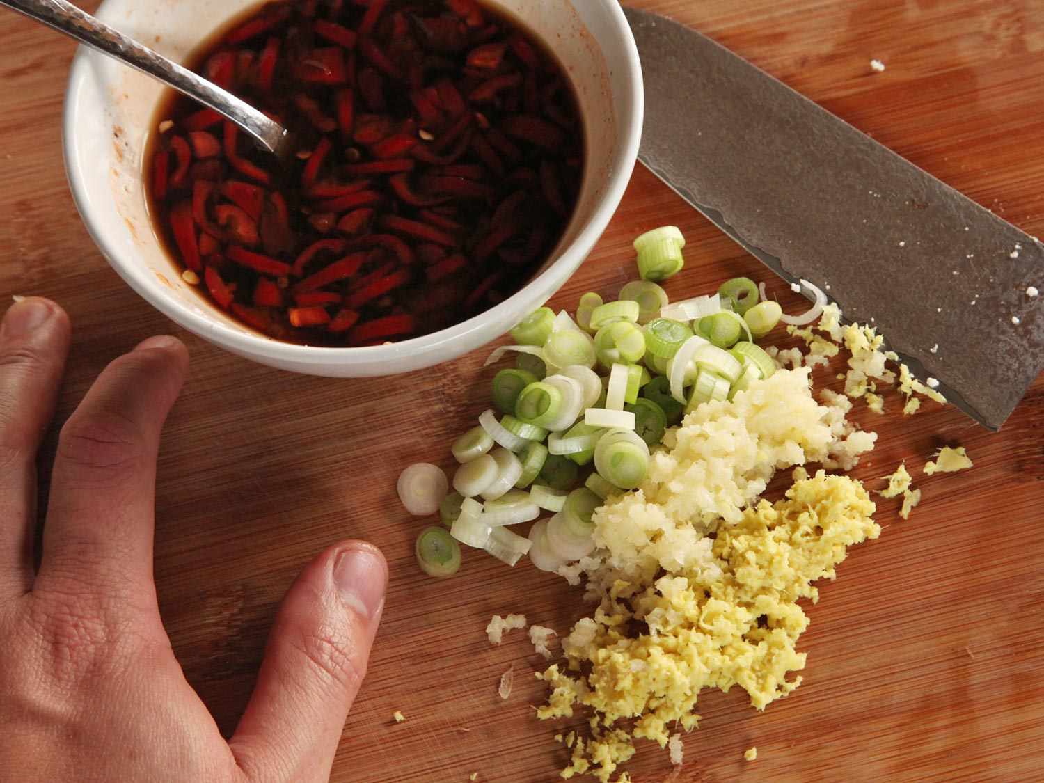 The pickled chiles and chili-bean paste are combined in a prep bowl, flanked by sliced scallions, minced garlic, and minced ginger.