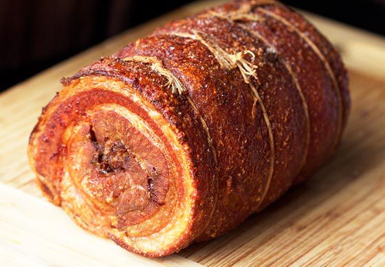 golden brown fried crispy pork belly porchetta on cutting board