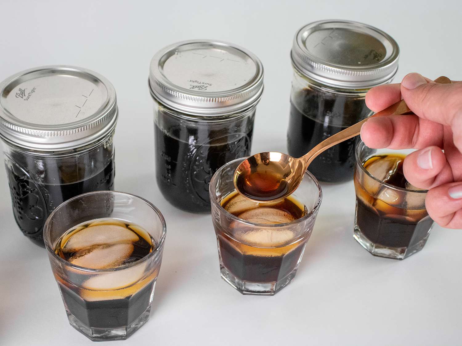 A person sampling a glass of cold brew with a cupping spoon.