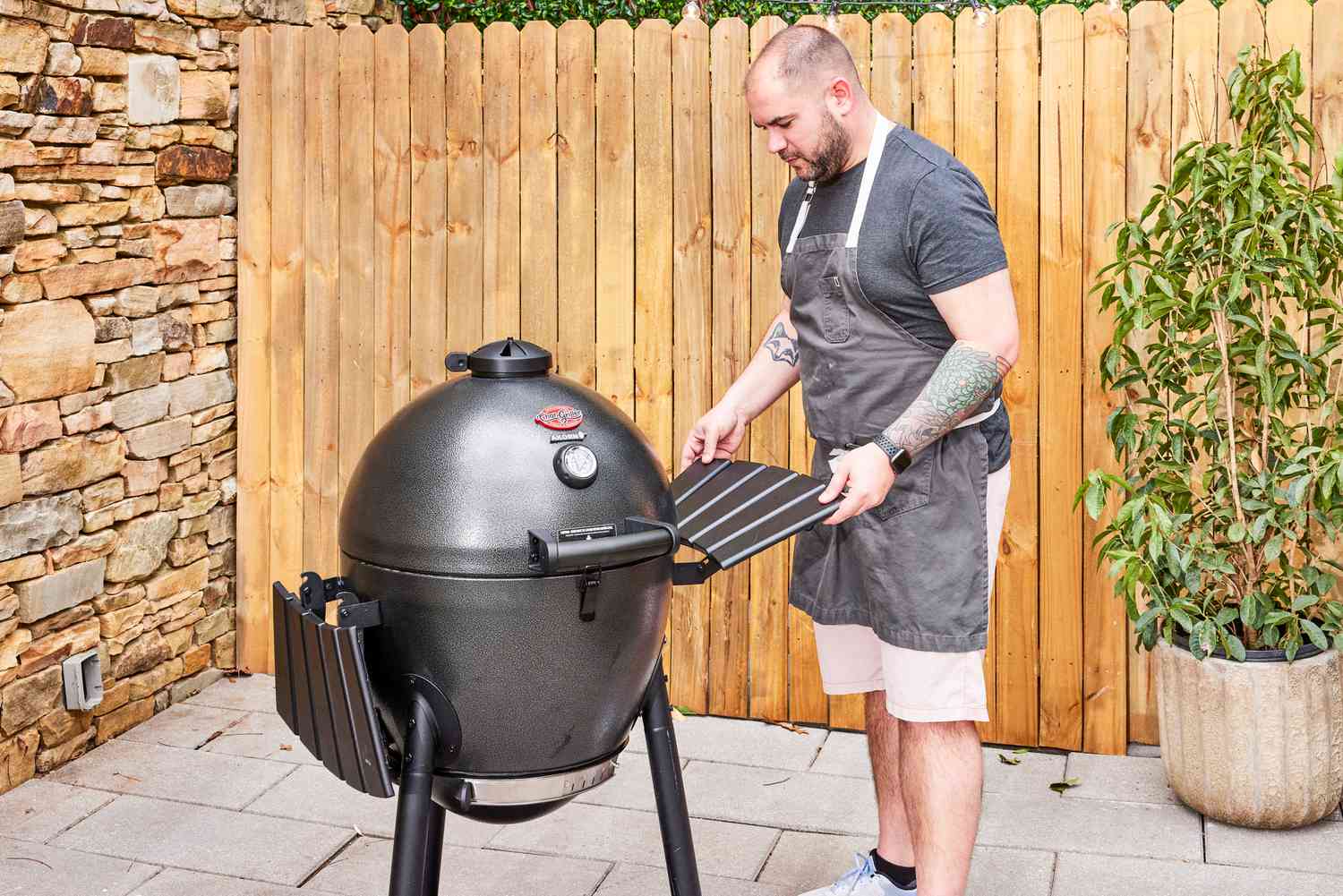 A person installs a shelf on the side of a Char-Griller E16620 Akorn Kamado Charcoal Grill