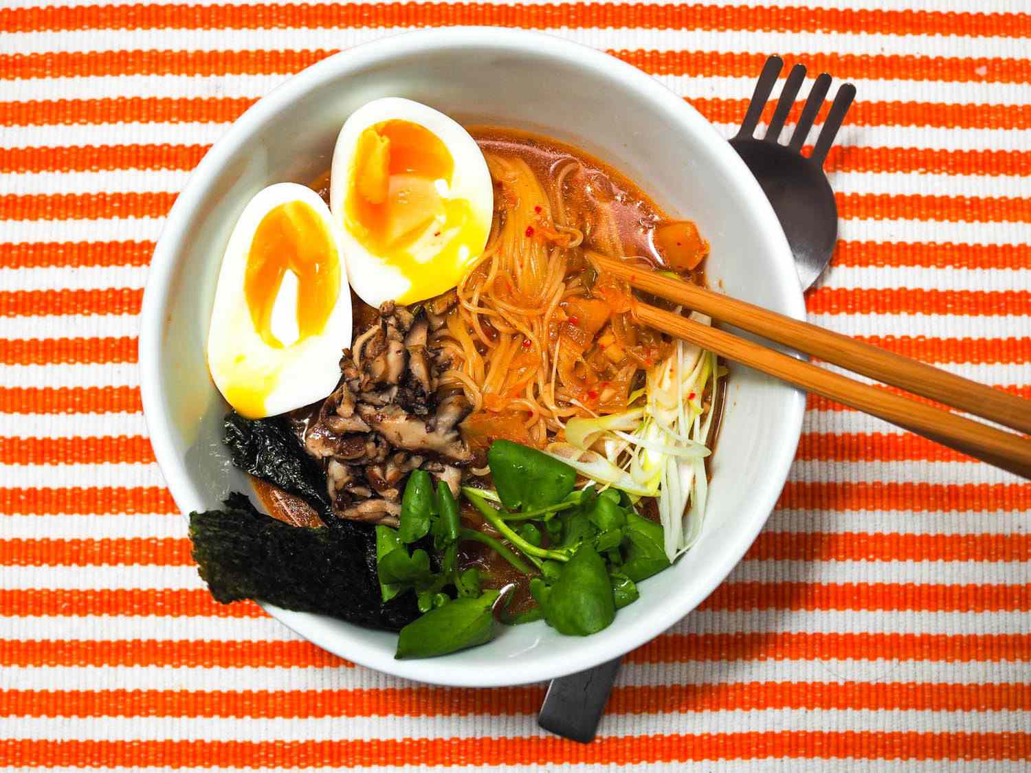 Overhead photo of ramen with soft boiled egg, on striped orange placemat.