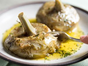 A plate of tender carciofi alla Romana. A fork easily cuts through a portion of one artichoke.