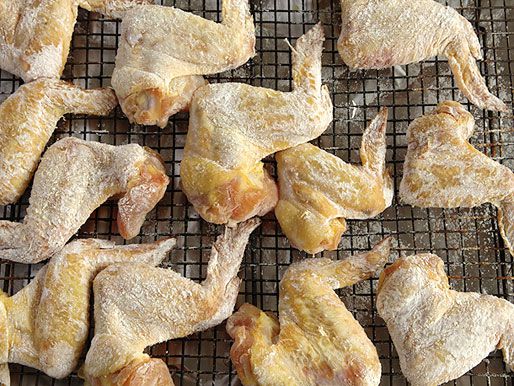 Twelve chicken wings salted and resting on a wine rack.