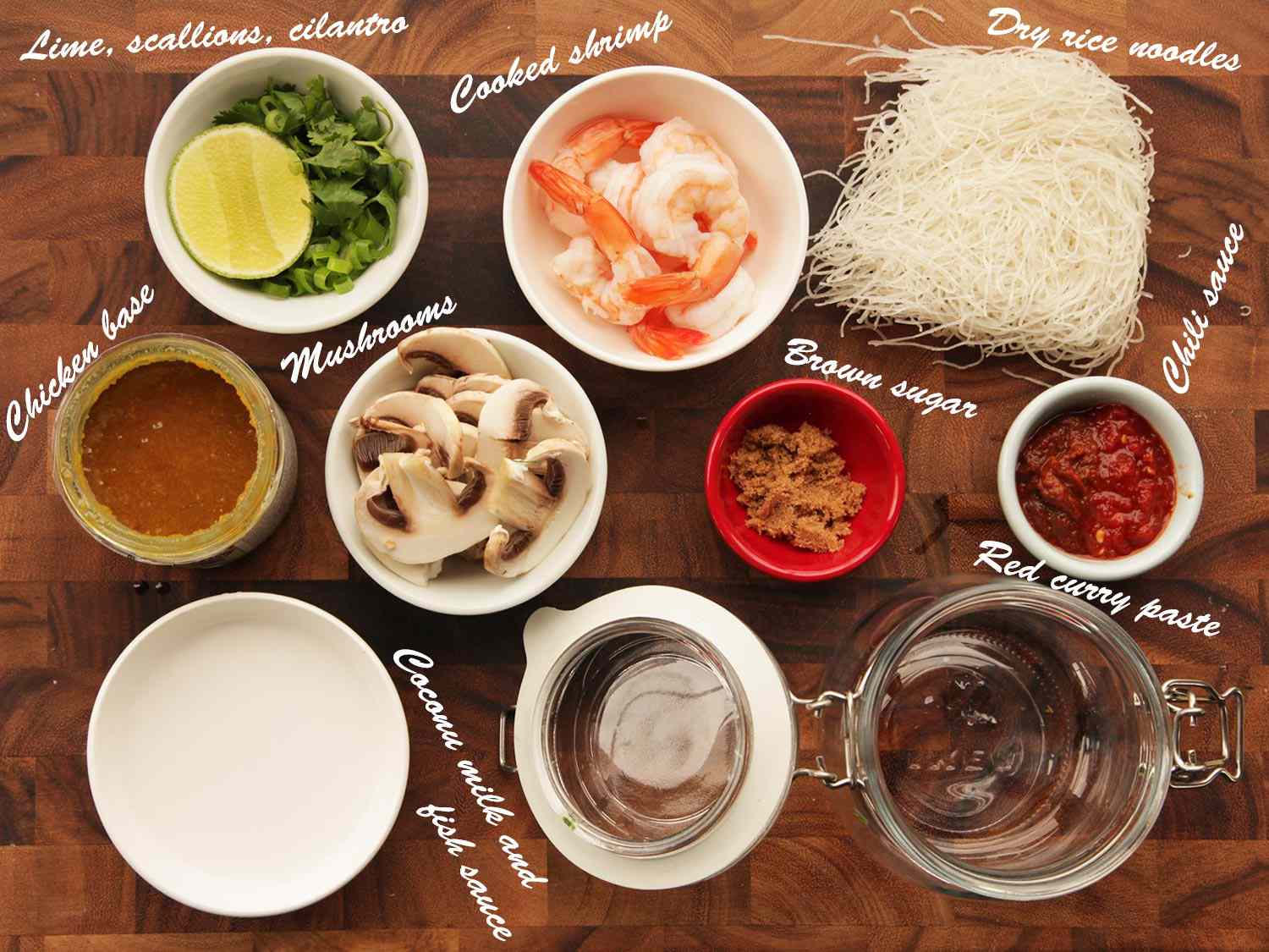 Overhead view of the ingredients for Thai coconut curry shrimp flavor instant noodles: lime, scallions, cilantro, cooked shrimp, dry rice noodles, chicken base, mushrooms, brown sugar, chile sauce, coconut milk and fish sauce.