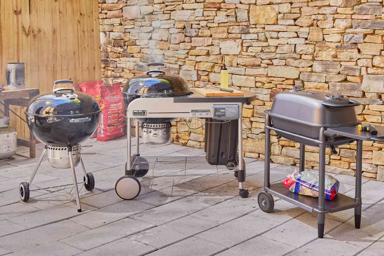 Three charcoal grills on an outdoor patio.