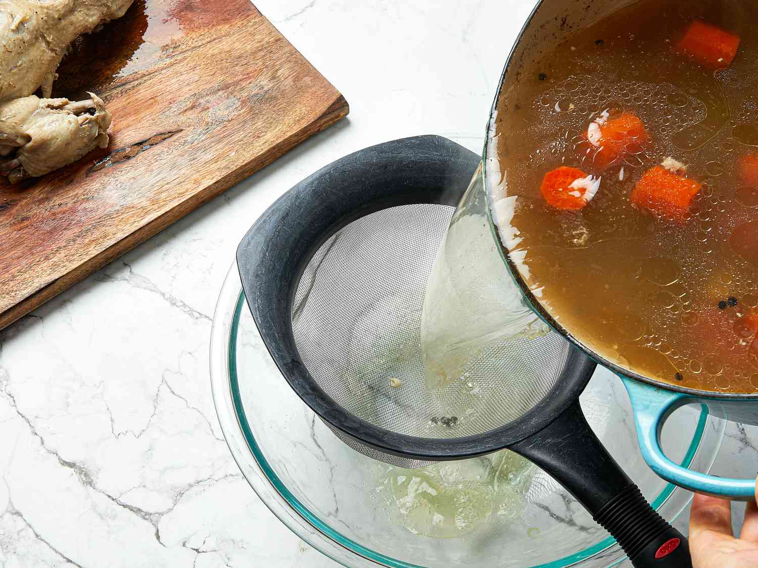 Pouring broth through a fine mesh sieve into a glass bowl 