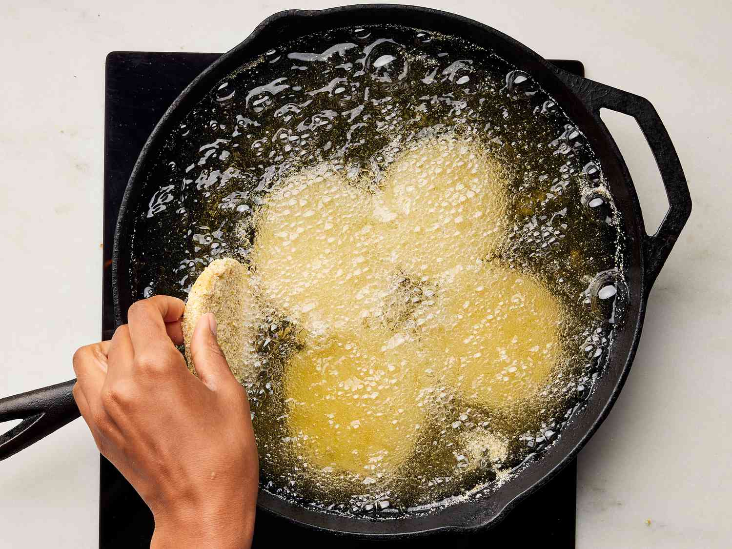 Hand dipping breaded green tomatoes into hot sizzling oil in a skillet 