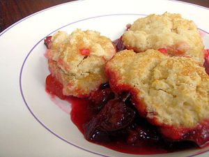 A large serving of plum and ginger cobbler plopped unto a white plate.