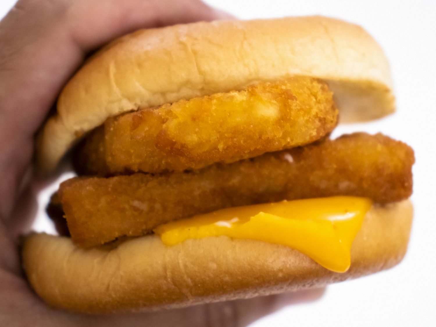 Hand gripping a McDonald's Filet-O-Fish with a hash brown slid inside