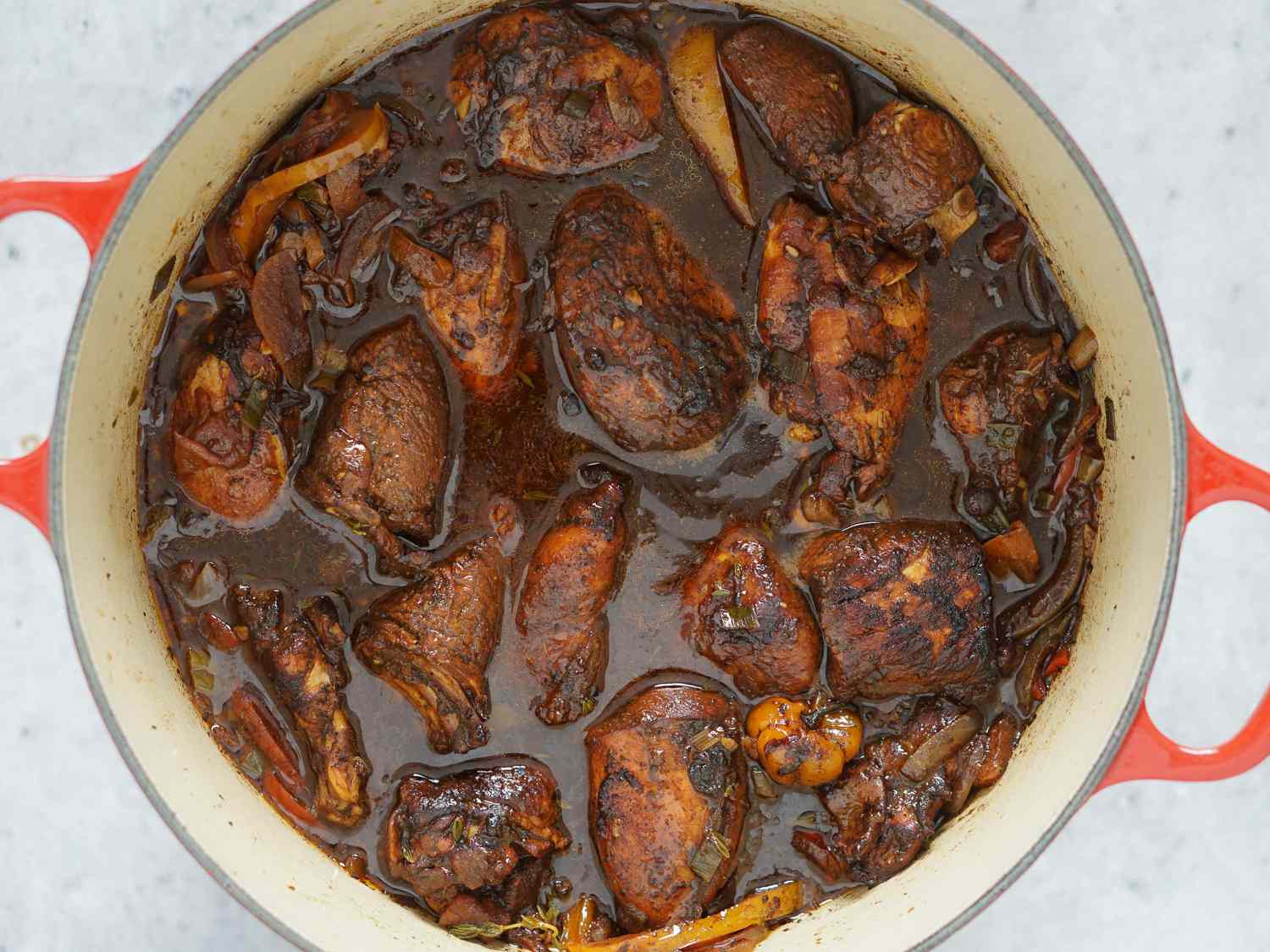 Dark chicken meat portions and breast portions tucked into brown stew chicken stewing liquid in Dutch oven