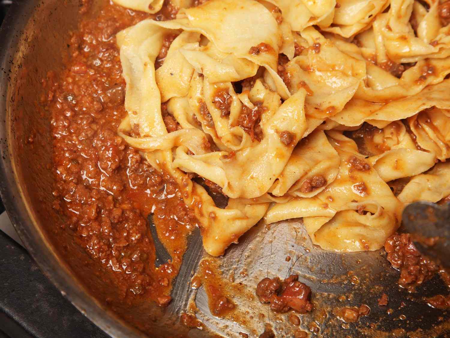 Cooked tagliatelle is tossed with the ragù Bolognese in a wide, sloped pan (sauteuse).