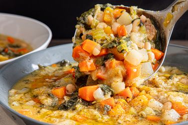A ladle lifting thick and chunky vegetable soup from a bowl