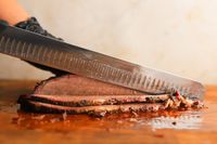 A person slicing meat using the Victorinox Fibrox Pro Slicing Knife