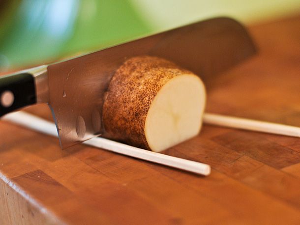 A potato is sliced between two chopsticks, thereby preventing the knife from going all the way through.