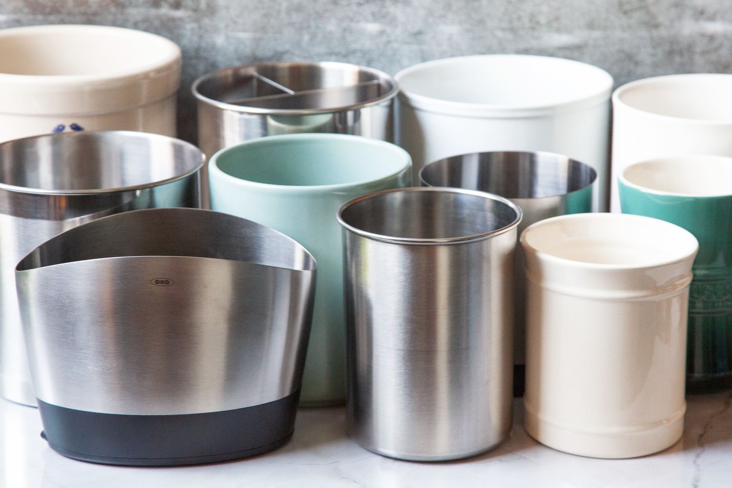 Numerous utensil crocks on a marble kitchen countertop.