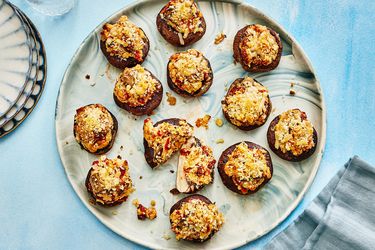 Vegetarian stuffed mushrooms on a blue and white platter, on top of a blue and white dyed surface. Serving plated and napkins to the side. 