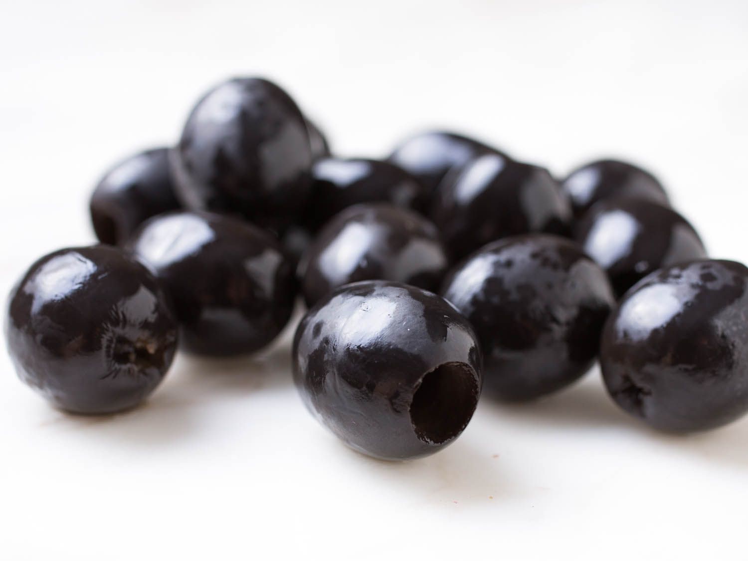 Pile of shiny, pitted, jet-black olives on white surface