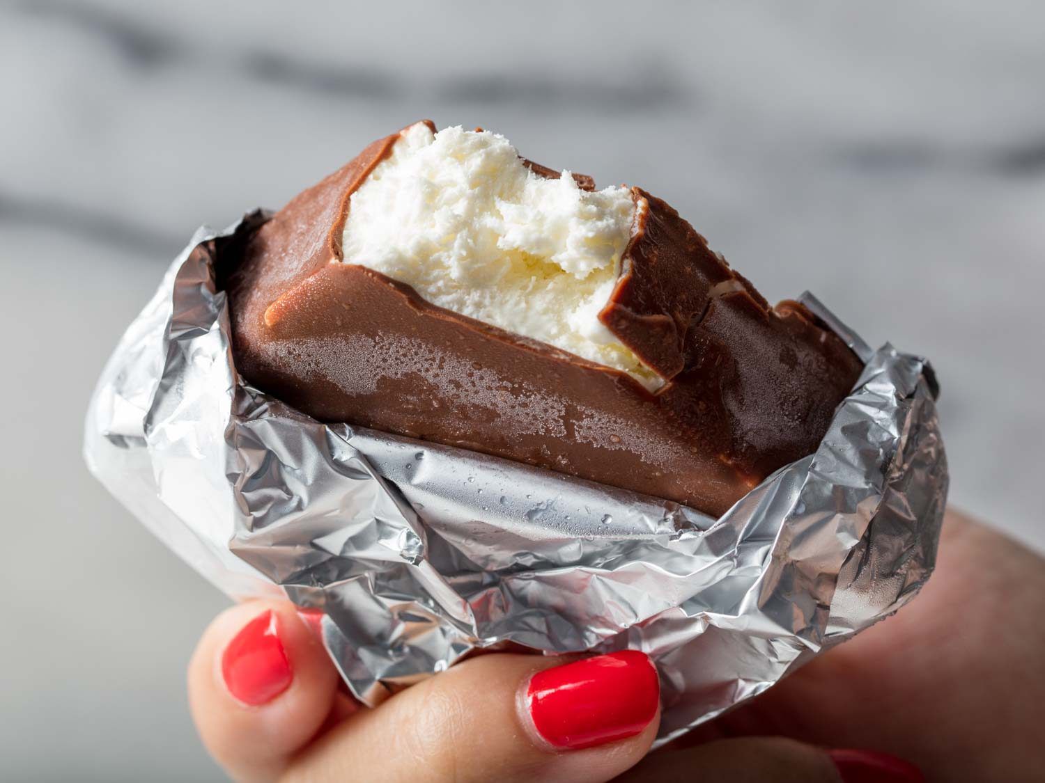 A hand holding a foil-wrapped homemade Klondike Bar with a bite taken out.