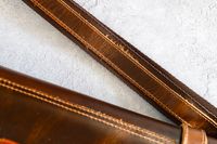 A closeup of a leather strap of Rustic Town Genuine Leather Chef Knife Roll with stitching on a textured background